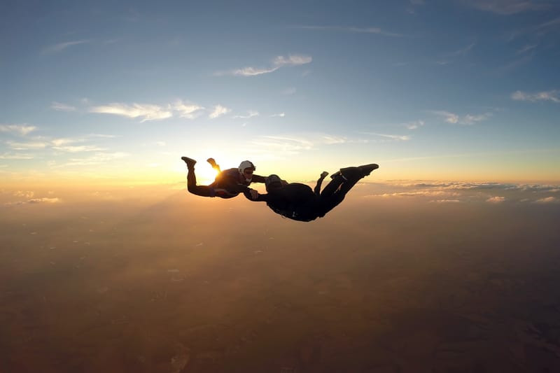 Experience your first solo skydive — AFF student and instructor freefalling at golden hour above the clouds.