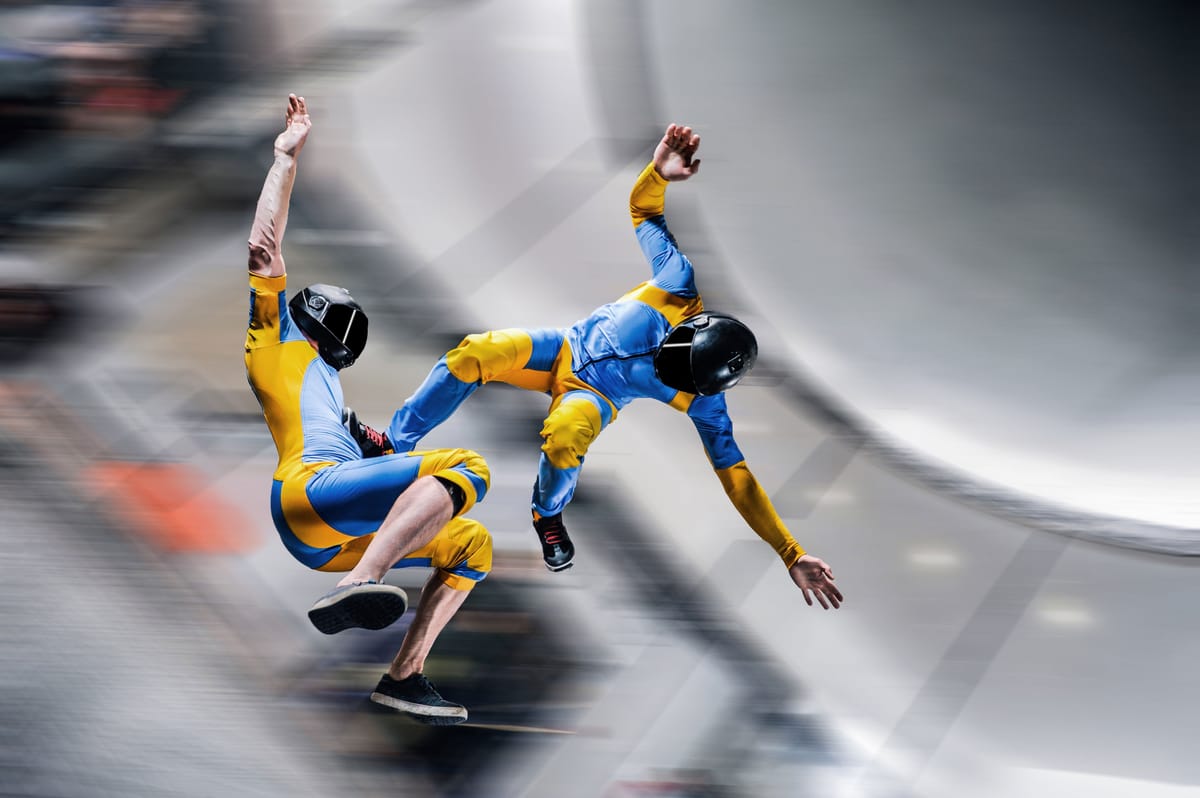 Indoor skydiving athletes in flight suits performing maneuvers in a vertical wind tunnel.