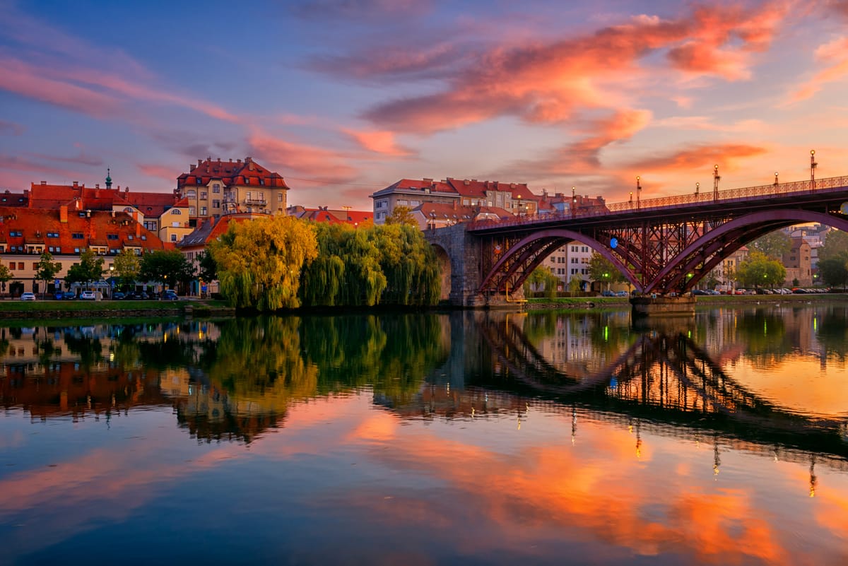 Sunset view of Maribor city center with the Drava River reflecting historic buildings and the Old Bridge, Slovenia.