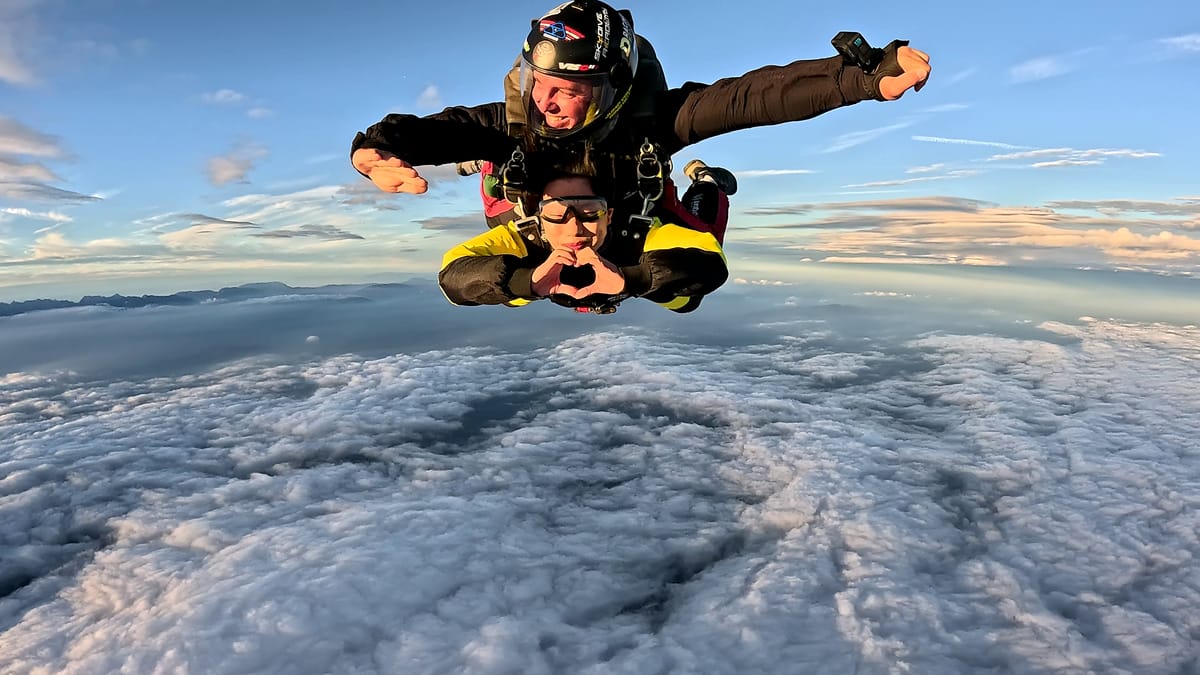 Grupni padobranski skok u slobodnom padu s plavim nebom, avionom iznad i slikovitim Slovenskim krajolikom ispod
