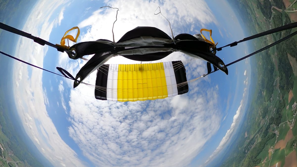 Close-up of deployed parachute during skydive with scenic landscape and blue skies in the background.
