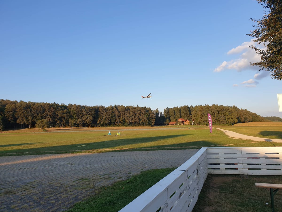 Light aircraft taking off at the Šentvid pri Stični dropzone in Slovenia, surrounded by open fields and forest.