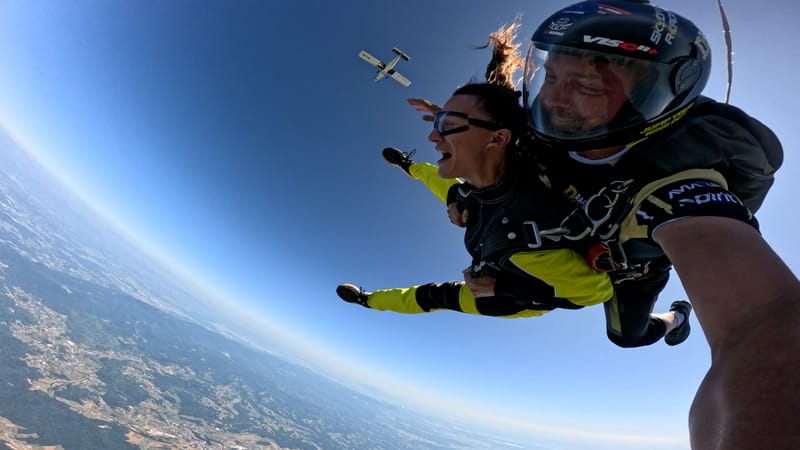 Excited tandem student with an instructor immediately after exit with plane above and panoramic landscape below