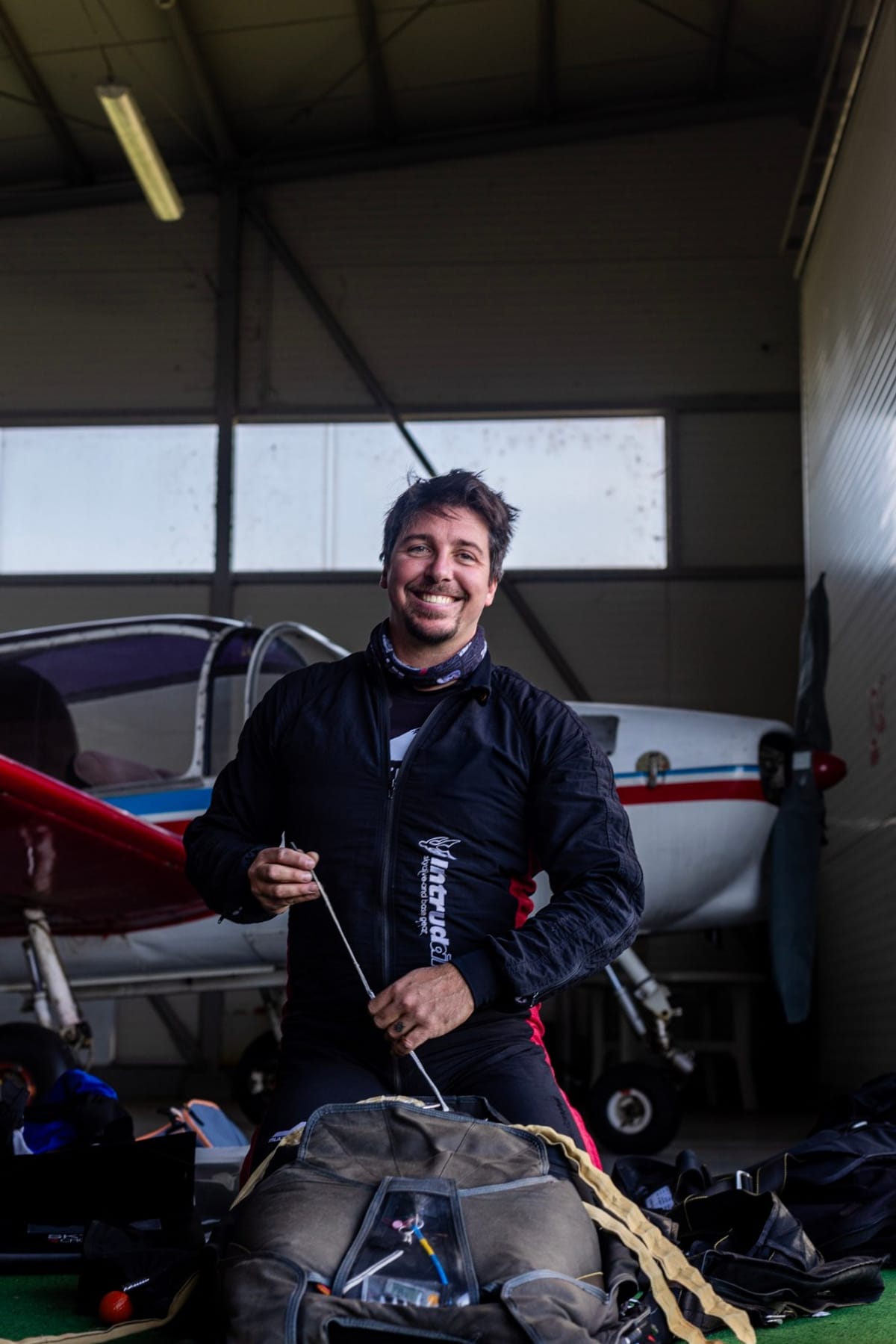 Marko Premužić, president of Skydive Academy, packing a parachute in a hangar in front of an aircraft.